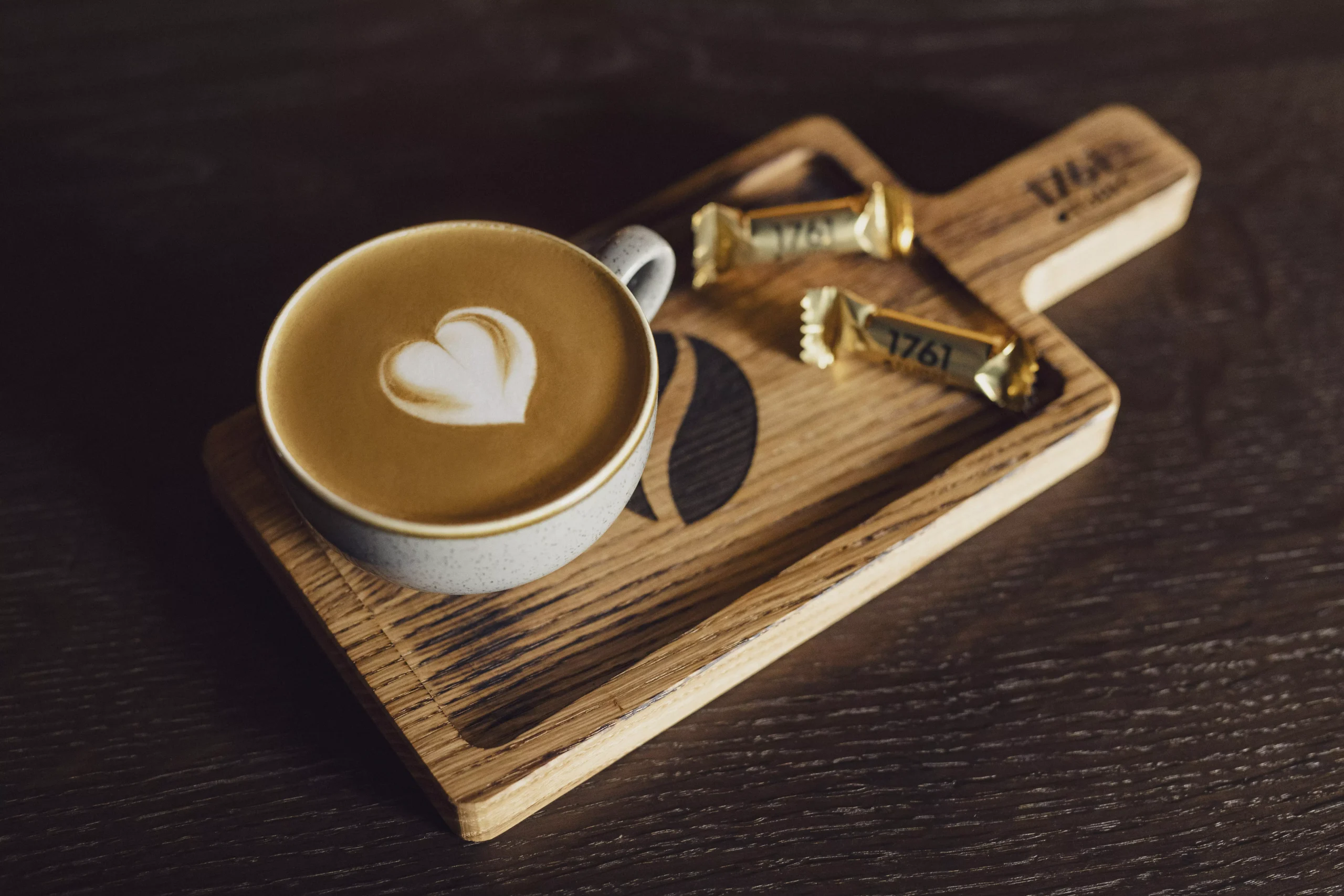 Cappucchinotasse mit Herzschaum auf einem Holzbrett mit zwei Schokosüssigkeiten